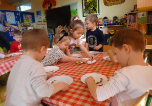 Dzieci układają kolorowe cukierki na brzegu talerzyków.
